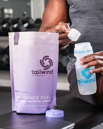 A person adding a scoop of Tailwind Nutrition Endurance Fuel to a water bottle.